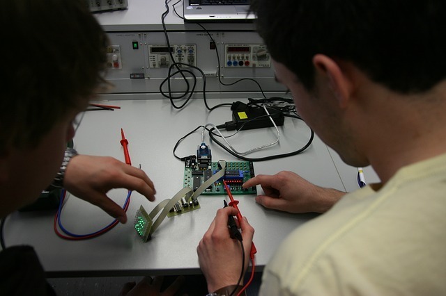 looking over the shoulders of two students working on an electronic circuit board