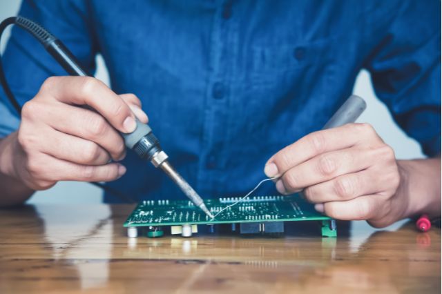 a close up of mens hands soldering on to an electronic circuit board