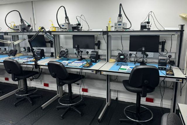 a row of 3 desks at an electronics training centre set up with equipment and IPC work books