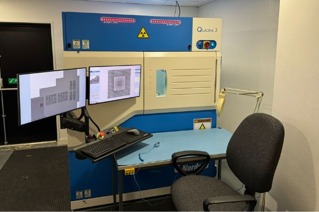 a desk chair facing two computer screens showing the x-ray images produced by the large non-destructive x-ray machine behind it