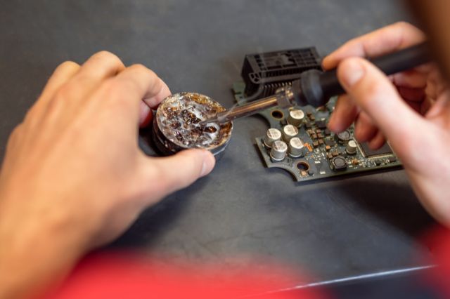 looking down on a pair of hands working with a hand soldering iron on a desk