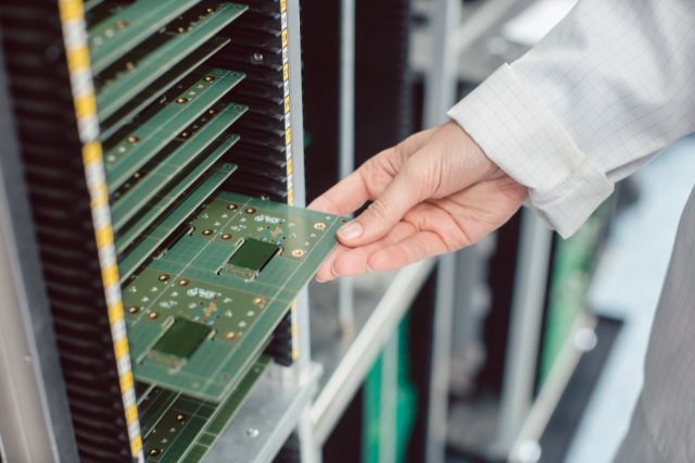 a hand pulling a large PCB from a storage wrack